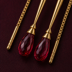 Detail close-up of dimensional sword charm and faceted briolette ruby in deep crimson on 18k gold threader.
